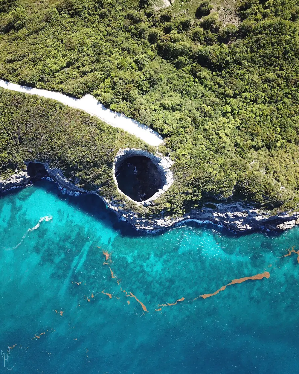Vue aérienne du gouffre circulaire ouvert dans la falaise boisée, au bord d'une mer turquoise