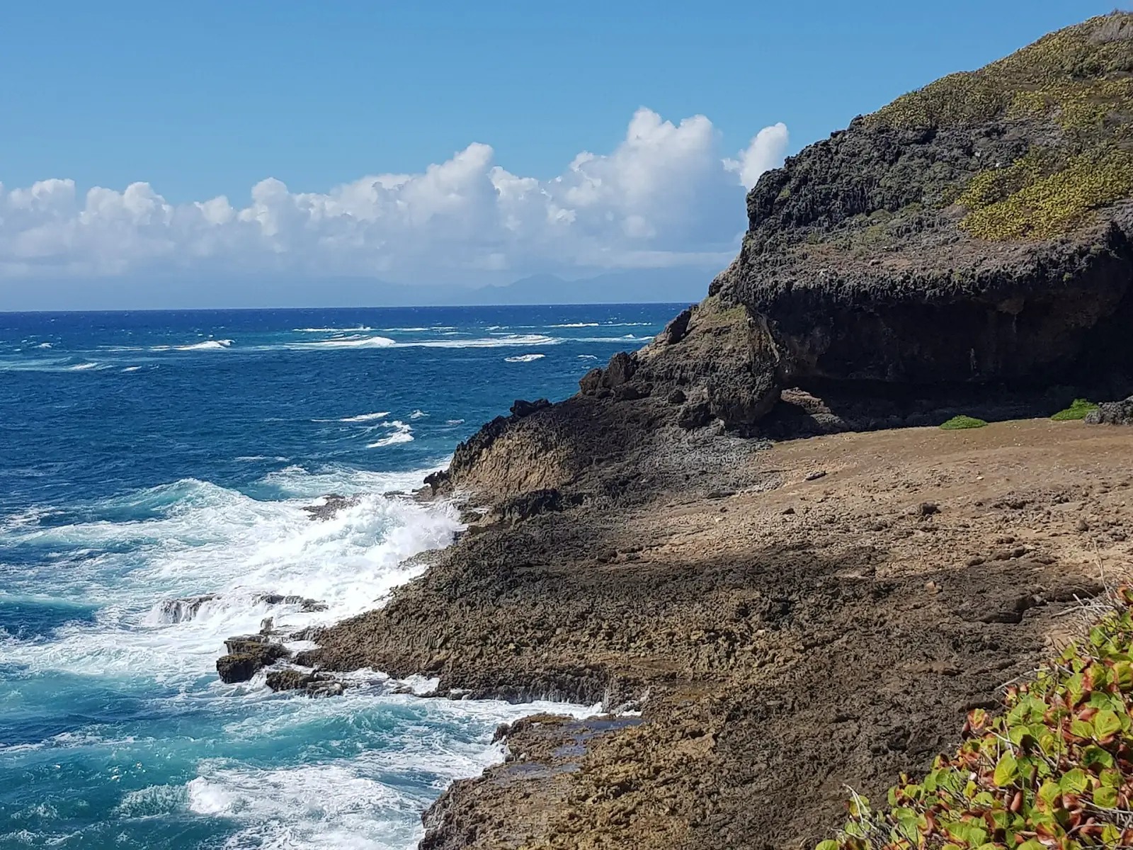 Une falaise sombre creusée par la mer au bord de l'océan agité, sous un ciel bleu