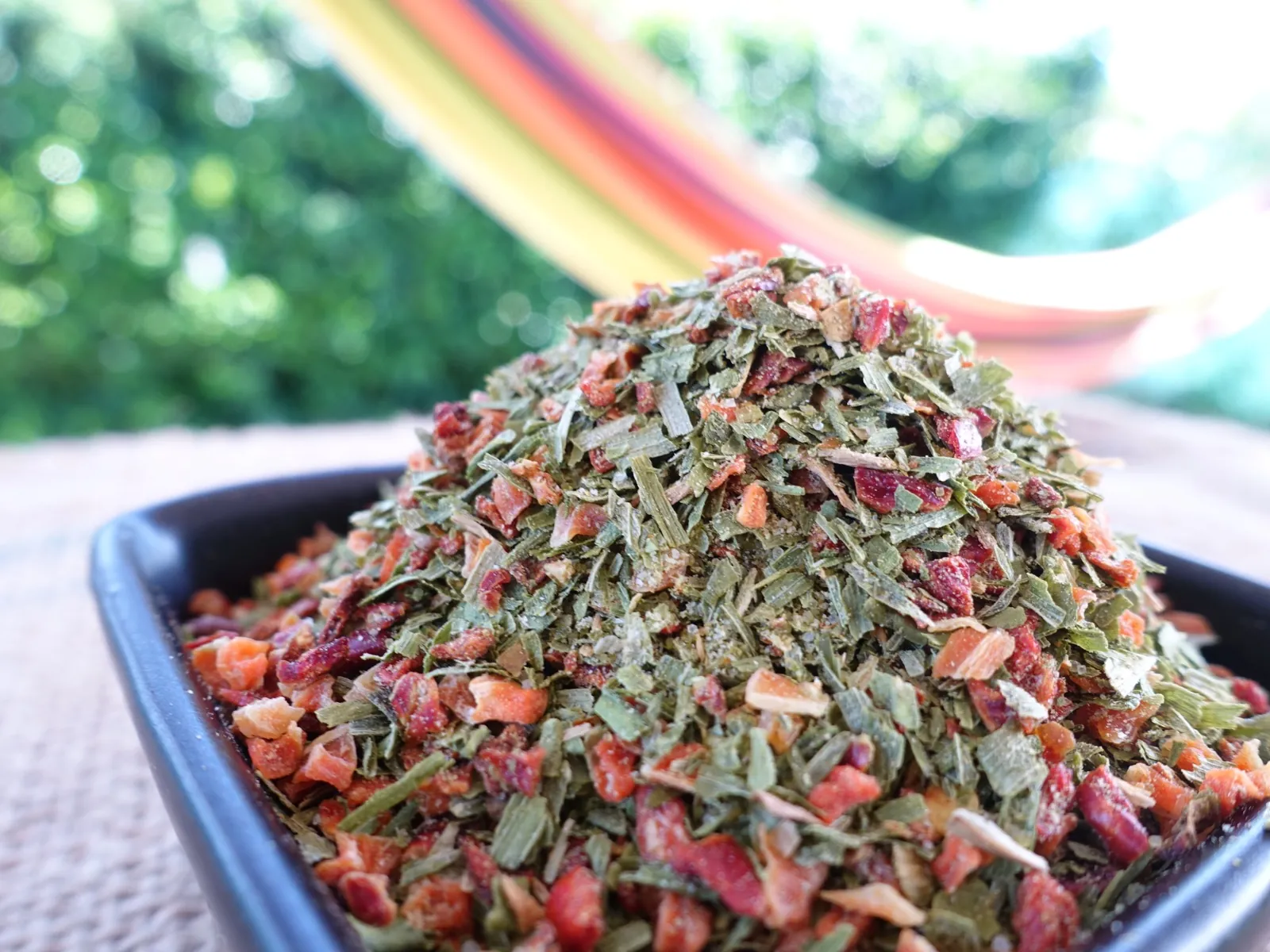 Un plat rempli d'un mélange d'épices séchées, herbes vertes et piment rouge, sur fond de tissu coloré